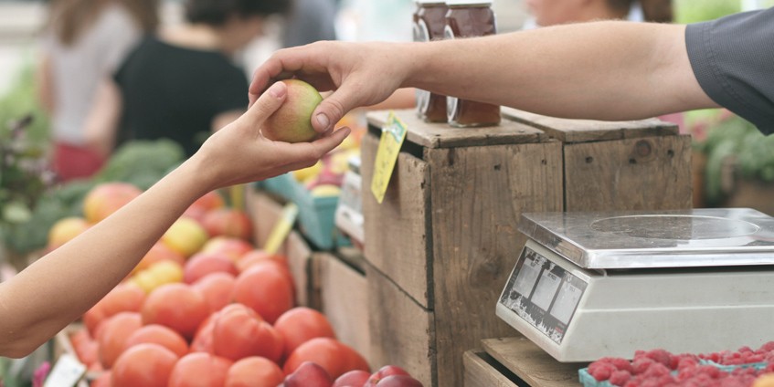 Two hands holding an apple at a fruit market.