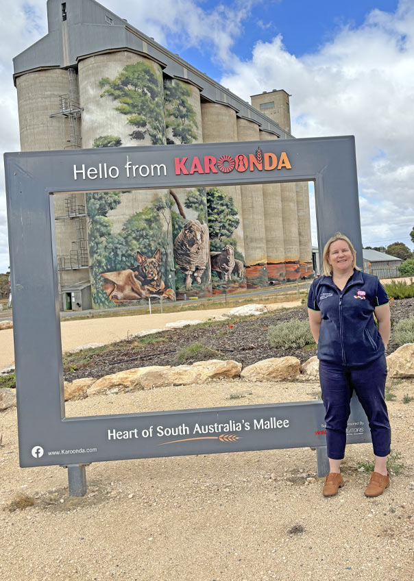 Dee-Anne Hull in front of mural painted silos with a sign saying hello from Karoonda