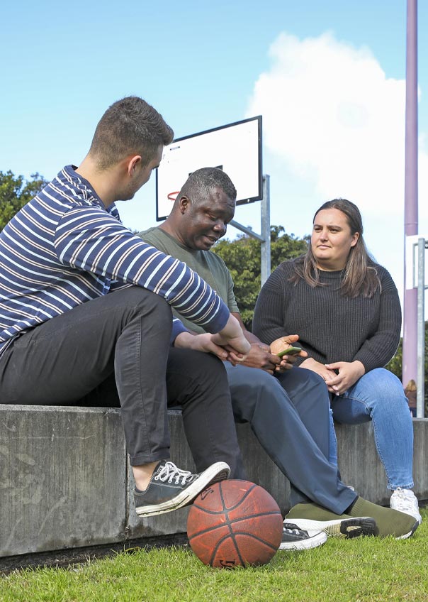 Three people talking seated on a basketball court