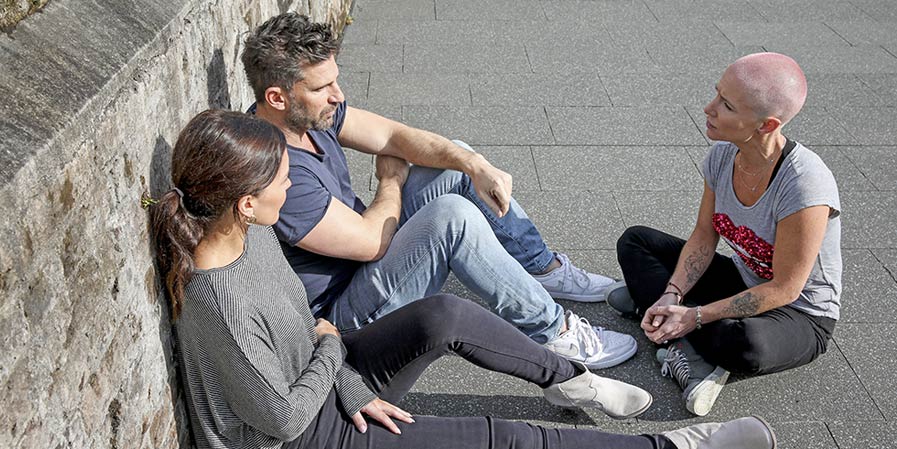 Three people seated on a park area talking