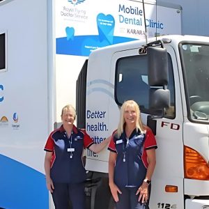 Two dental works standing in front of a mobile dental clinic truck