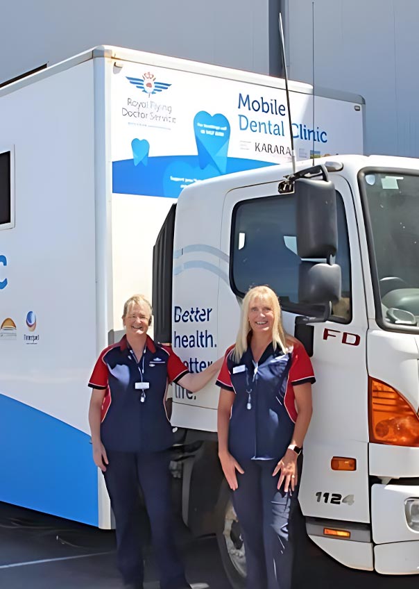 Two dental works standing in front of a mobile dental clinic truck