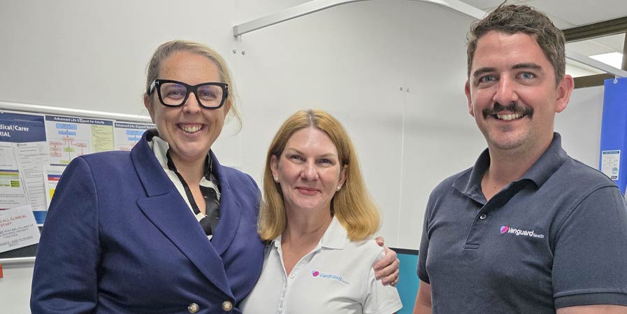 Three people posing for phot in medical room.