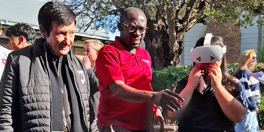 Image caption: A student explores rural practice through a virtual reality headset at the 2025 Western Sydney University Open Day in Parramatta, as the University Chancellor watches on. Photo credit: Bathurst Rural Clinical School