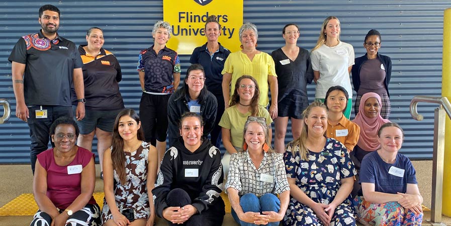 Large group of people posing for photo in front of sign Flinders University