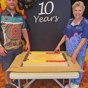 Two people on either side of large cake with sign saying saying 10 Years