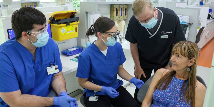 Dental clinic patient in a chair with three detail practitioners