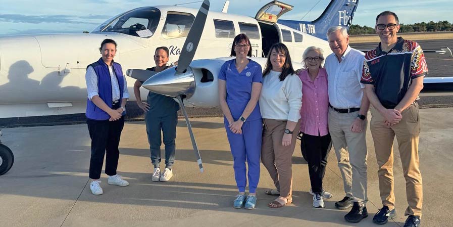 Seven people stand in front of a propellor driver Angel Flight aircraft