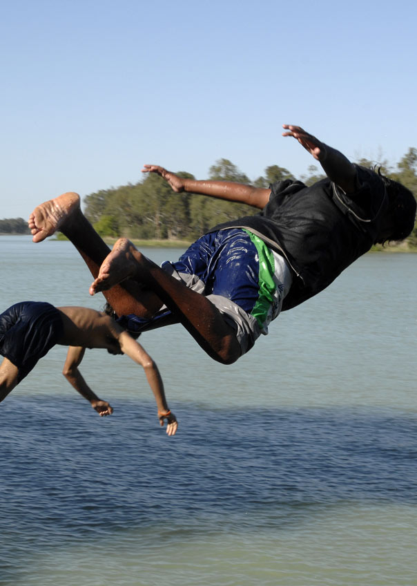Three children jumping into a river from a bridge